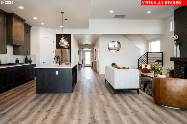 kitchen featuring sink, stainless steel appliances, wall chimney range hood, light hardwood / wood-style flooring, and a kitchen island with sink