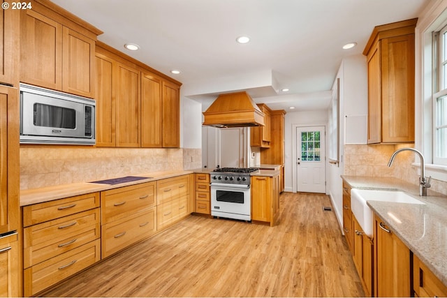 kitchen featuring high end white range, stainless steel microwave, sink, custom range hood, and light hardwood / wood-style flooring