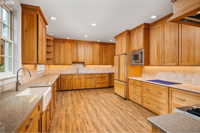 kitchen with built in appliances, sink, light stone countertops, backsplash, and light wood-type flooring