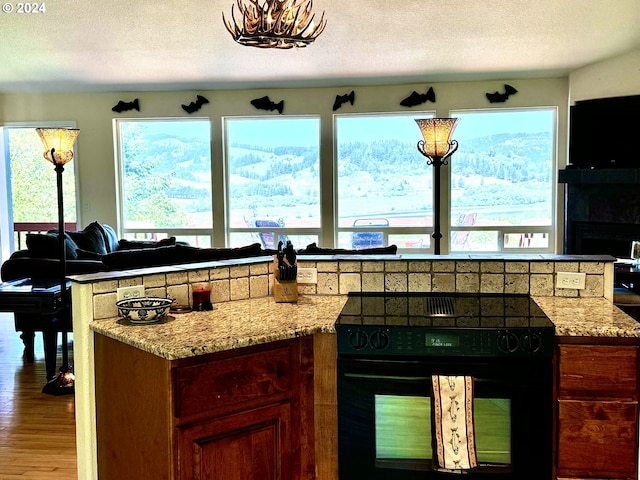 kitchen with black range with electric stovetop, hardwood / wood-style floors, light stone counters, and a textured ceiling