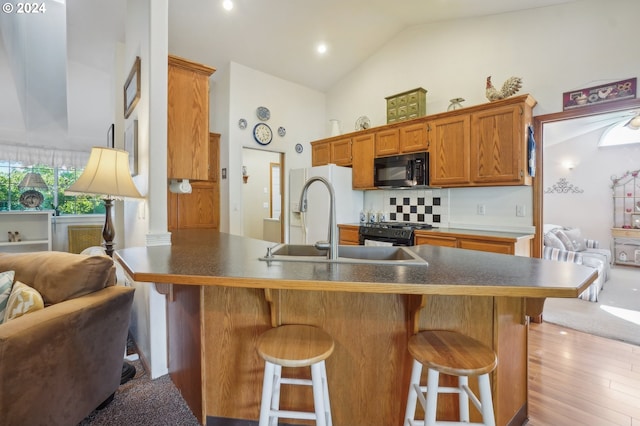 kitchen featuring sink, a kitchen breakfast bar, high vaulted ceiling, tasteful backsplash, and black appliances