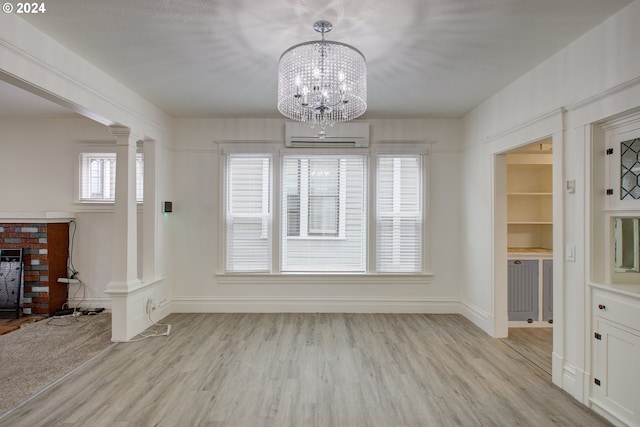 unfurnished dining area featuring an inviting chandelier, light hardwood / wood-style floors, decorative columns, and a wall unit AC