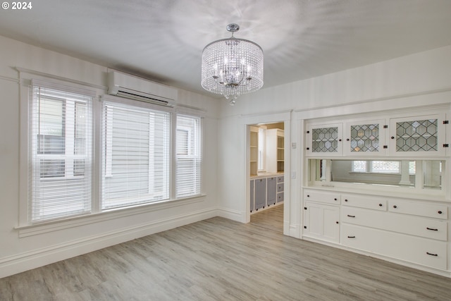 unfurnished dining area with light wood finished floors, a chandelier, a wall mounted AC, and baseboards