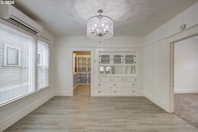 unfurnished dining area featuring a wall mounted air conditioner, light hardwood / wood-style flooring, and a chandelier