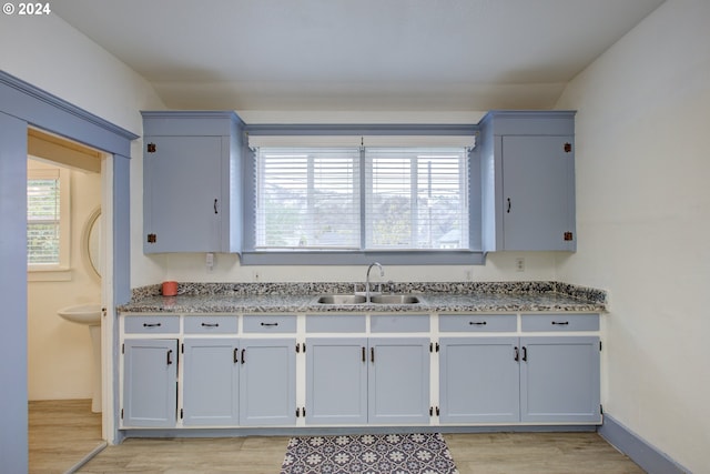 kitchen with light wood-style flooring, light stone counters, baseboards, and a sink