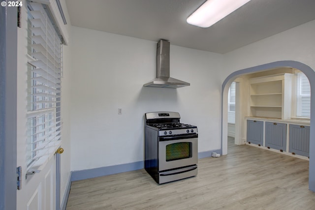 kitchen with baseboards, stainless steel range with gas cooktop, wall chimney exhaust hood, and light wood finished floors