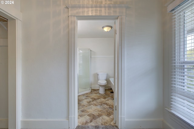 bathroom with baseboards, a shower stall, toilet, and stone finish floor