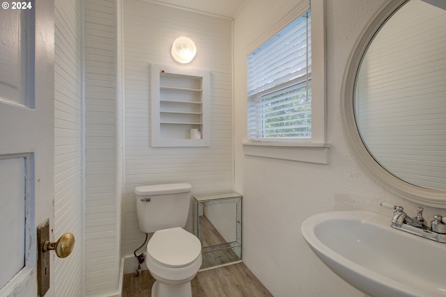 bathroom featuring toilet, wood finished floors, a textured wall, and a sink