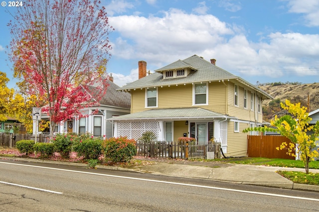 traditional style home with a fenced front yard, a porch, and roof with shingles