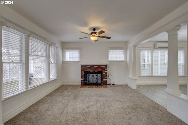 unfurnished living room featuring a brick fireplace, light colored carpet, a wall unit AC, and ornate columns