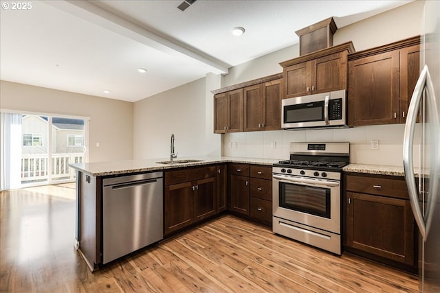 kitchen featuring stainless steel appliances, light wood-style flooring, a sink, light stone countertops, and a peninsula