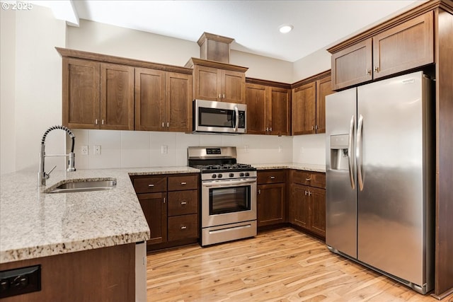 kitchen with light stone counters, stainless steel appliances, a sink, light wood-style floors, and decorative backsplash