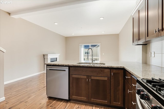 kitchen featuring appliances with stainless steel finishes, light wood-style floors, a sink, dark brown cabinets, and a peninsula