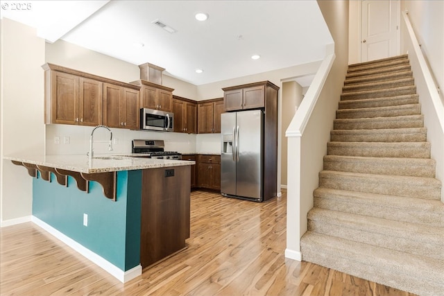 kitchen featuring light wood finished floors, visible vents, appliances with stainless steel finishes, a peninsula, and a sink