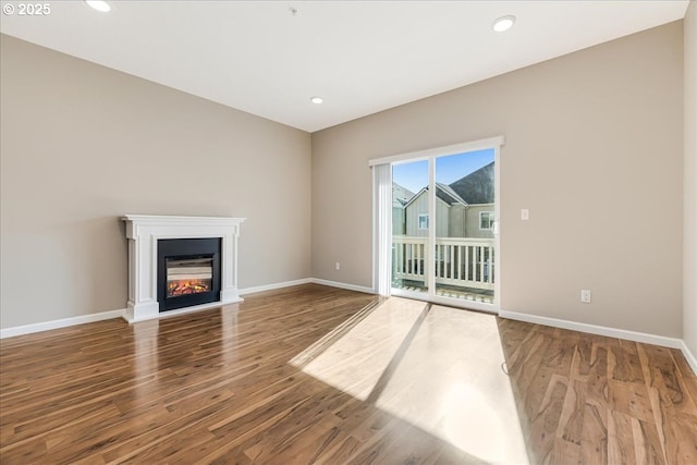 unfurnished living room with a glass covered fireplace, recessed lighting, baseboards, and wood finished floors