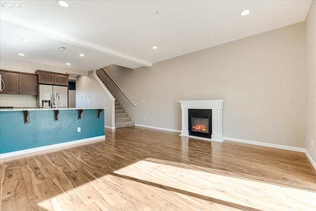 unfurnished living room featuring light wood-style floors, baseboards, stairway, and recessed lighting