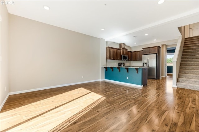 unfurnished living room with stairs, recessed lighting, wood finished floors, and baseboards