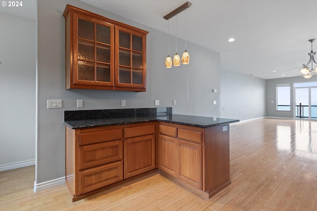 kitchen featuring glass insert cabinets, pendant lighting, brown cabinets, dark stone countertops, and light wood-style floors