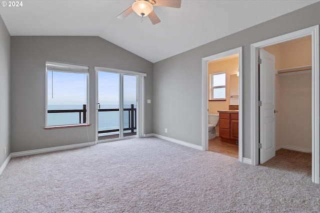 unfurnished bedroom featuring carpet, baseboards, lofted ceiling, a walk in closet, and access to outside