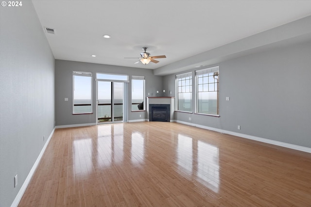 unfurnished living room featuring ceiling fan, a water view, and light wood-type flooring