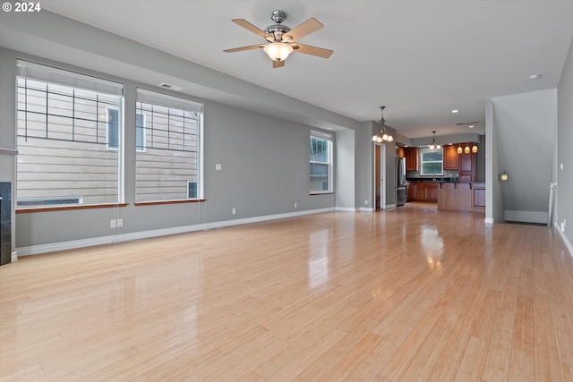 unfurnished living room featuring visible vents, baseboards, light wood-style floors, and ceiling fan with notable chandelier