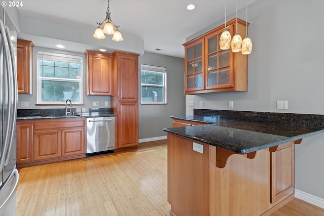 kitchen featuring brown cabinets, light wood-style flooring, a sink, appliances with stainless steel finishes, and a peninsula