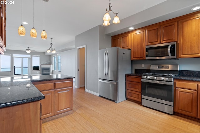 kitchen with brown cabinetry, light wood-style flooring, a fireplace, appliances with stainless steel finishes, and pendant lighting