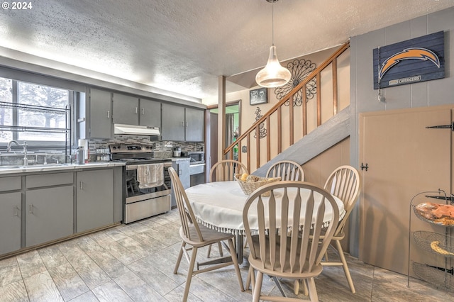 kitchen with a textured ceiling, decorative light fixtures, sink, and stainless steel range with electric cooktop