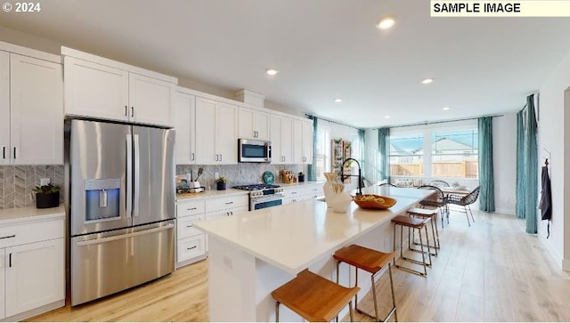 kitchen with white cabinetry, a center island with sink, light wood-type flooring, and appliances with stainless steel finishes