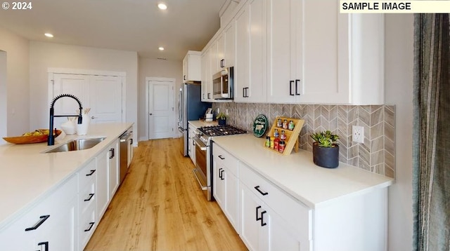 kitchen featuring appliances with stainless steel finishes, backsplash, sink, white cabinets, and light hardwood / wood-style floors