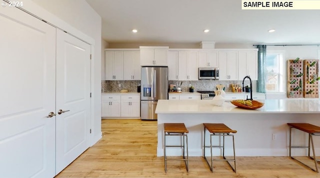 kitchen featuring sink, appliances with stainless steel finishes, light hardwood / wood-style floors, a kitchen bar, and white cabinetry