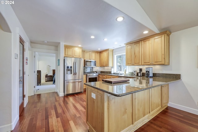 kitchen featuring dark stone countertops, appliances with stainless steel finishes, kitchen peninsula, and dark hardwood / wood-style flooring