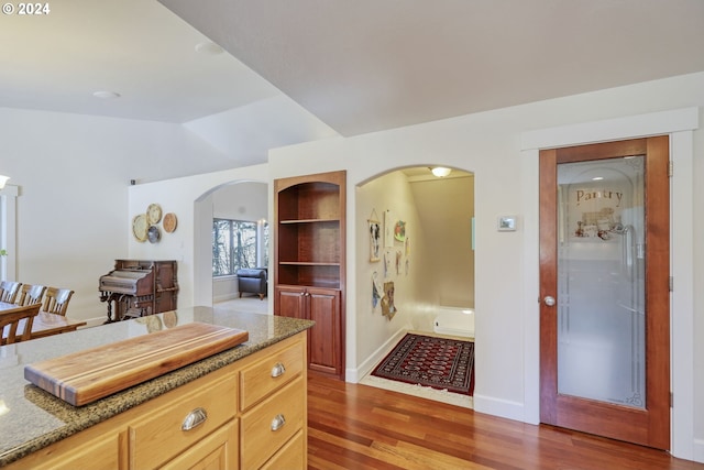 kitchen featuring lofted ceiling, light stone counters, light brown cabinetry, and dark wood-type flooring