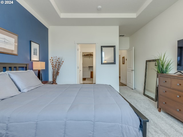 carpeted bedroom with a raised ceiling and a walk in closet