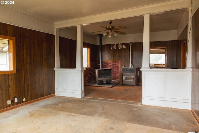 unfurnished living room featuring a wood stove, plenty of natural light, and wooden walls