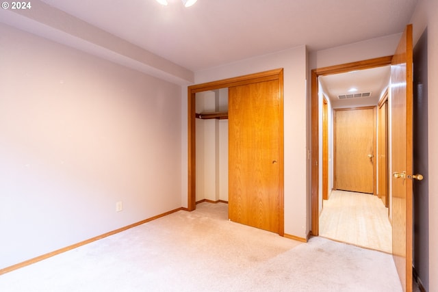 unfurnished bedroom with light colored carpet and a closet