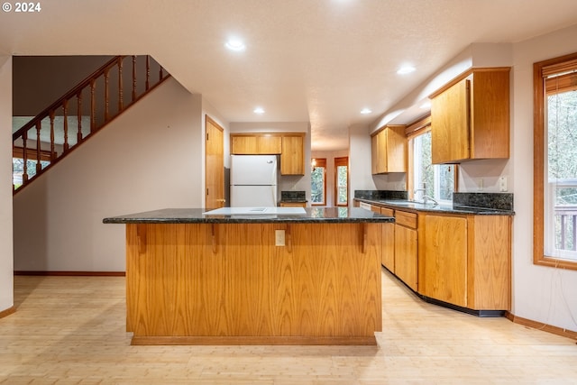 kitchen with a center island, dark stone counters, white refrigerator, sink, and light wood-type flooring