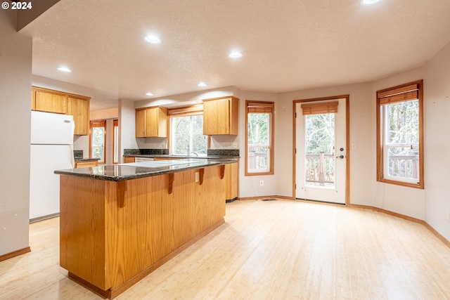 kitchen featuring light wood-type flooring, a textured ceiling, white refrigerator, and a kitchen island