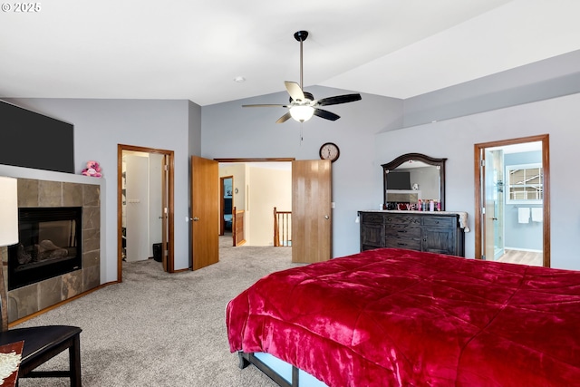 carpeted bedroom with ceiling fan, connected bathroom, vaulted ceiling, and a tiled fireplace