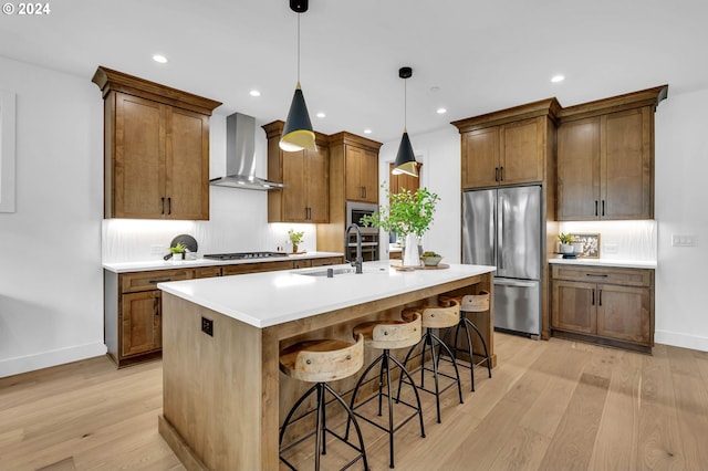 kitchen featuring stainless steel appliances, decorative light fixtures, a kitchen breakfast bar, wall chimney range hood, and a kitchen island with sink