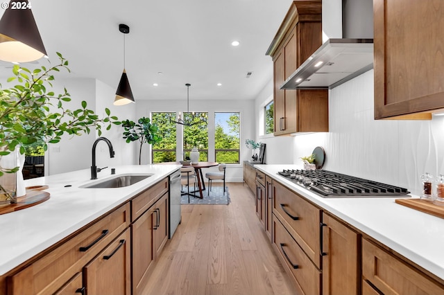 kitchen with light hardwood / wood-style floors, hanging light fixtures, appliances with stainless steel finishes, sink, and wall chimney range hood