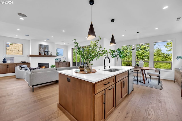 kitchen with a kitchen island with sink, light hardwood / wood-style floors, sink, decorative light fixtures, and stainless steel dishwasher