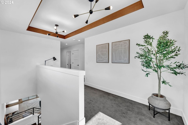 interior space featuring an inviting chandelier, a raised ceiling, and dark colored carpet