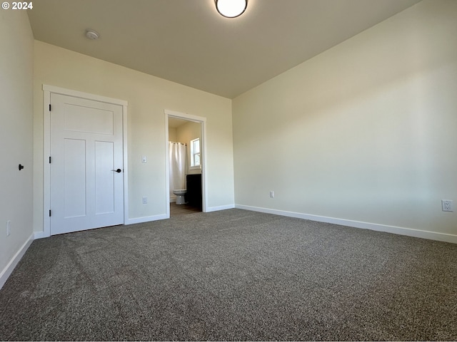 unfurnished bedroom featuring dark carpet and ensuite bath