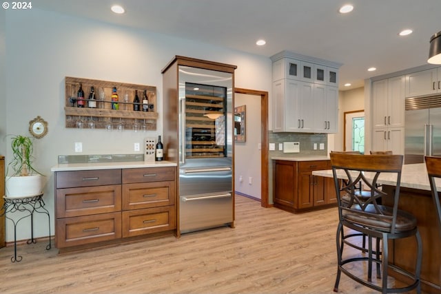 kitchen with light countertops, glass insert cabinets, light wood-type flooring, and backsplash