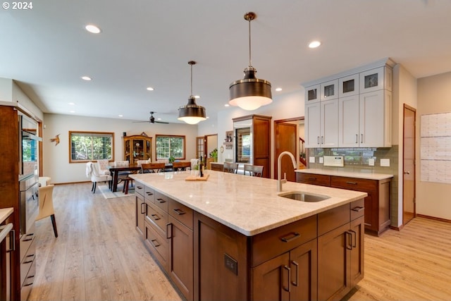 kitchen with a center island with sink, a sink, decorative backsplash, glass insert cabinets, and light wood-style floors