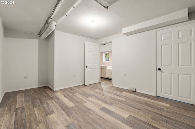 unfurnished bedroom featuring a textured ceiling, connected bathroom, and light hardwood / wood-style flooring