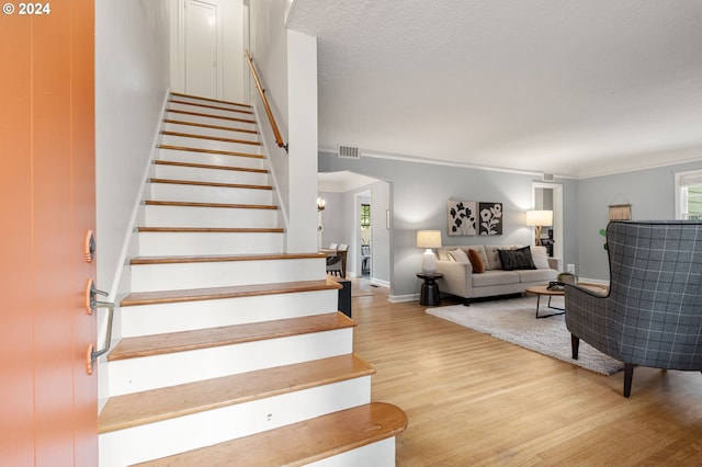 stairs with a textured ceiling, hardwood / wood-style flooring, and crown molding