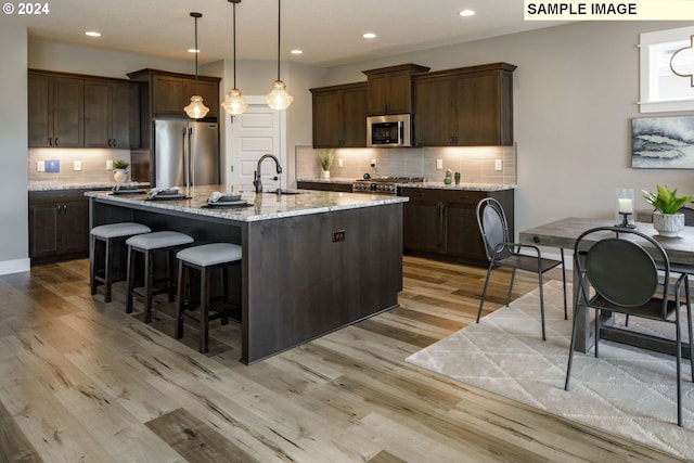 kitchen with light stone countertops, appliances with stainless steel finishes, light wood-type flooring, sink, and a center island with sink