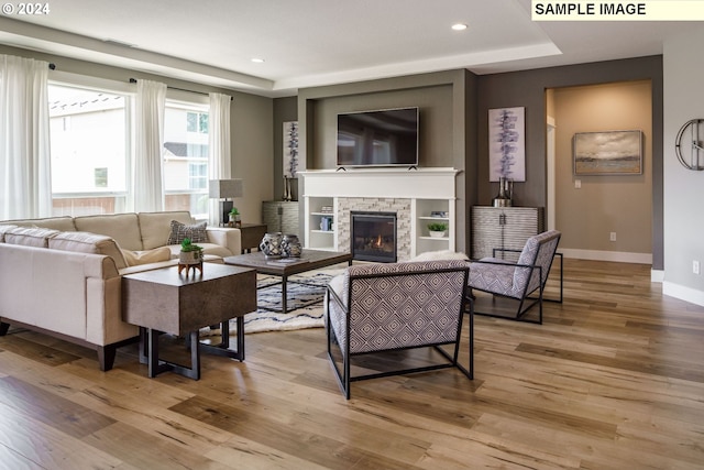 living room with light hardwood / wood-style floors, a stone fireplace, and a tray ceiling